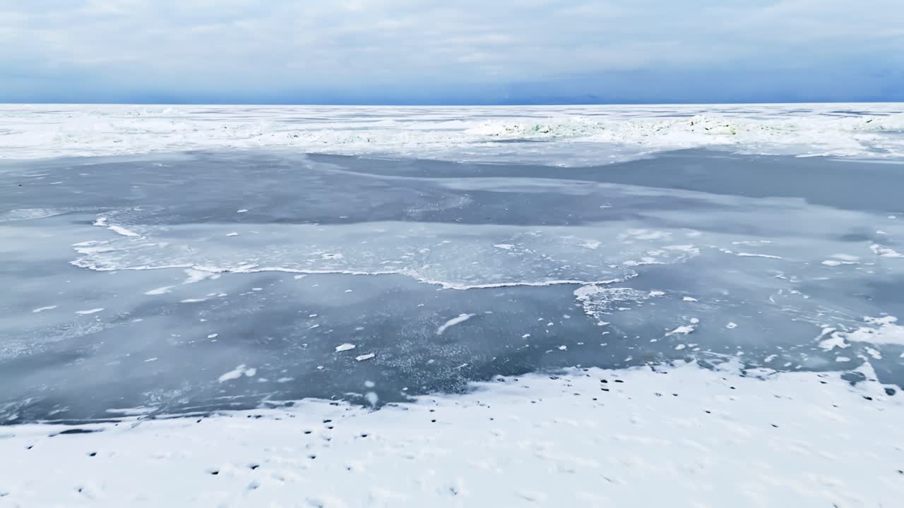 Sorvolo con drone sopra un mare ghiacciato e coperto di neve, con canali di ghiaccio scuro e una zona d'acqua parzialmente aperta, che cattura aspre texture invernali e condizioni climatiche remote e fredde.