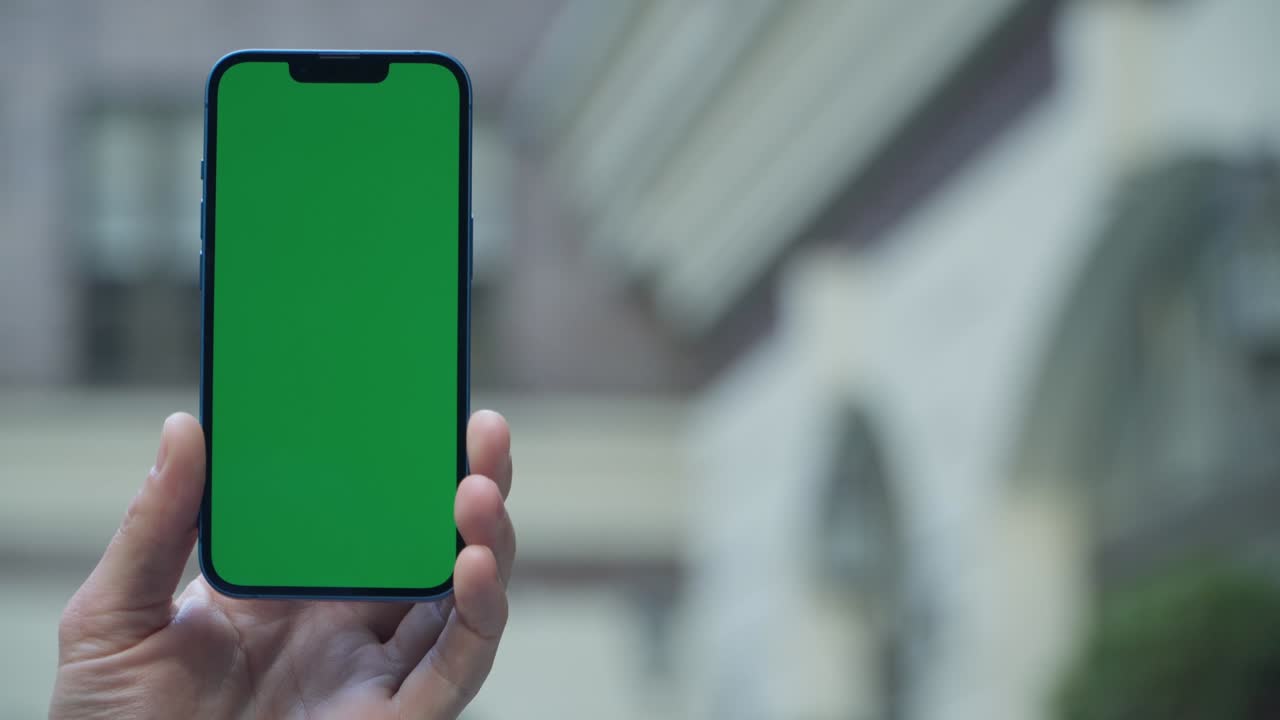 close-up de 4k de la mano de un hombre sosteniendo un teléfono inteligente con pantalla verde en una calle de la ciudad