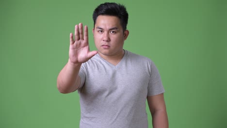 young handsome overweight asian man against green background