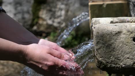 Mujer-Lavándose-Las-Manos-Con-Agua-Corriente-De-Manantial-En-Una-Antigua-Fuente-De-Agua