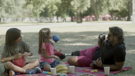 dad taking photo of kids inflating balloons at picnic