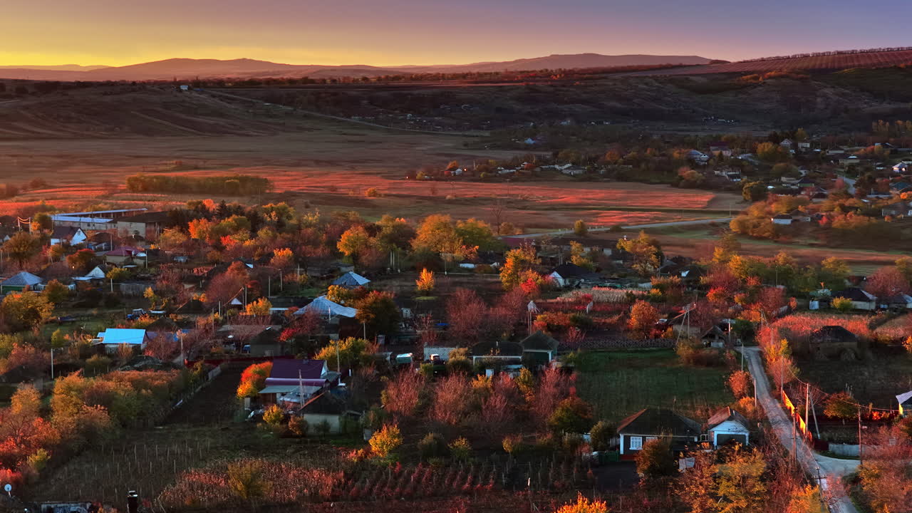 Aerial drone view of a Moldovan village surrounded by autumn trees and farmlands during sunset