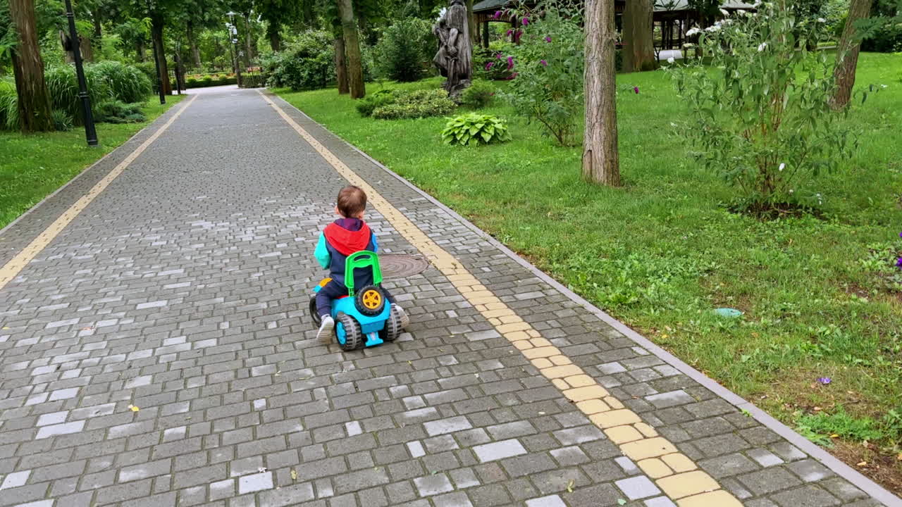 Beautiful smiling kid riding toy car cheerfully. Happy child is on the walk in autumn.