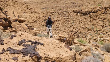 un hombre excursionista con palos de excursionismo caminando por la pendiente escarpada de piedra arenisca durante un viaje en el sendero del cráter ramon, desierto del negev, israel