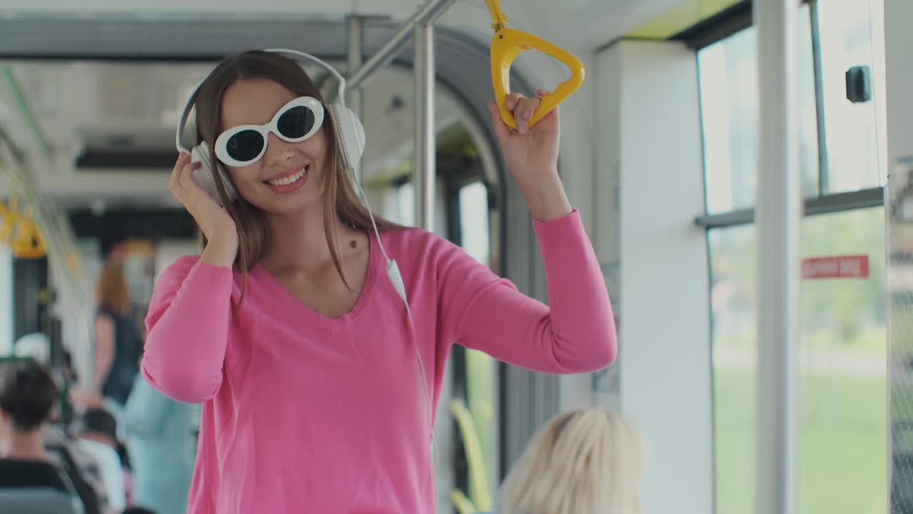 retrato en primer plano de una mujer joven con auriculares de pie en el tranvía moderno. una mujer con gafas escucha música en un tranvía.