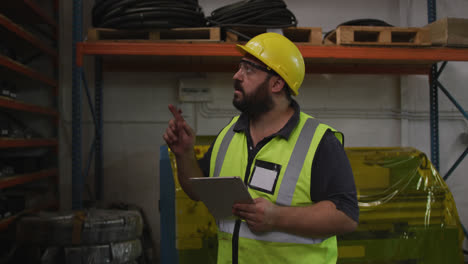 Caucasian-male-factory-worker-at-a-factory,-wearing-a-hat-and-glasses,-checking-stock