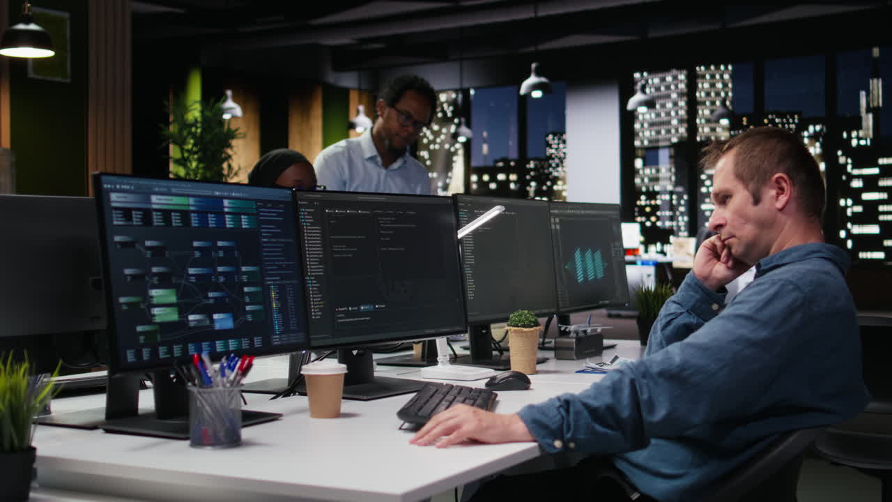 Male Programmer Working Late Night on Multiple Computer Monitors in Office