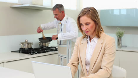 businesswoman using laptop while husband cooks dinner