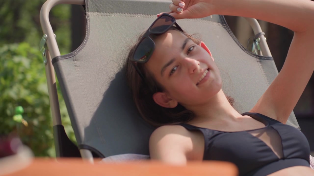 Woman relaxes on sun lounger with fresh fruit and orange juice in foreground. scene features soft natural light outdoor greenery and calm composition details