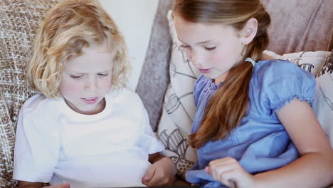 siblings sitting on the couch while using a tablet computer