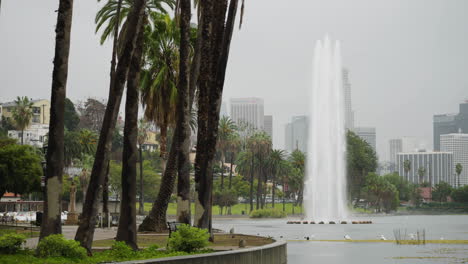 a wide shot of echo park lake in heavy rain with the dtla skyline and palm trees