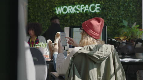 young-business-woman-using-smartphone-browsing-project-information-on-mobile-phone-screen-reading-research-study-statistics-brainstorming-ideas-relaxing-feet-on-table-in-modern-office