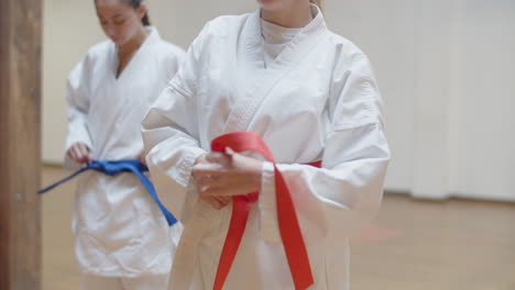 front view of focused girls tying orange and blue belts on kimonos