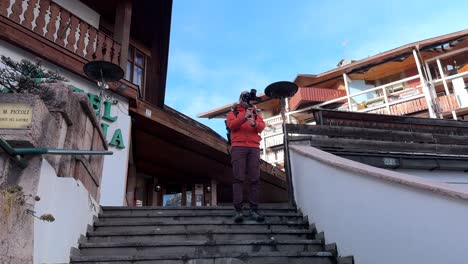 travel photographer with camera on gimbal stabilizer standing on stairs, taking photos in cortina d'ampezzo, italy