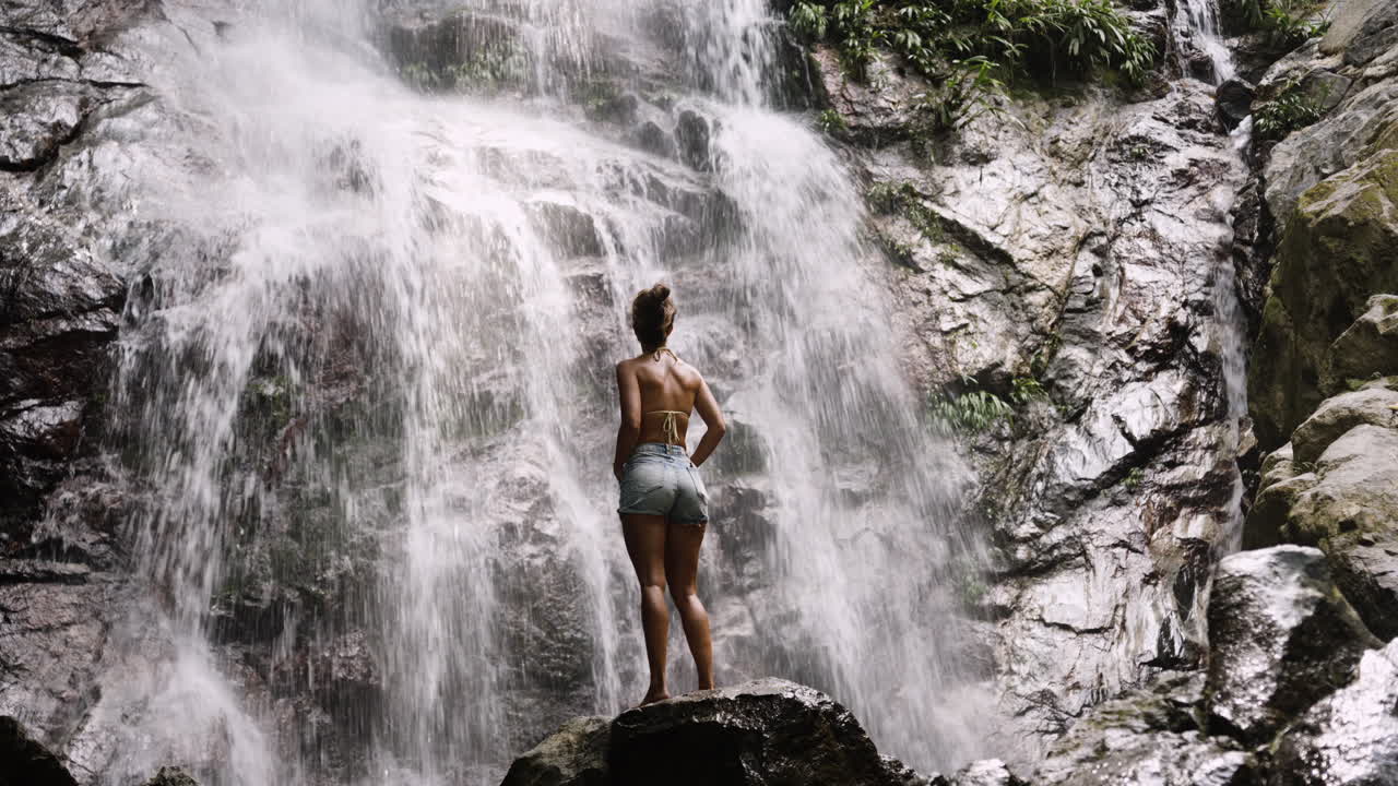 Girl at waterfall, mist rising around her in lush Colombian jungle setting