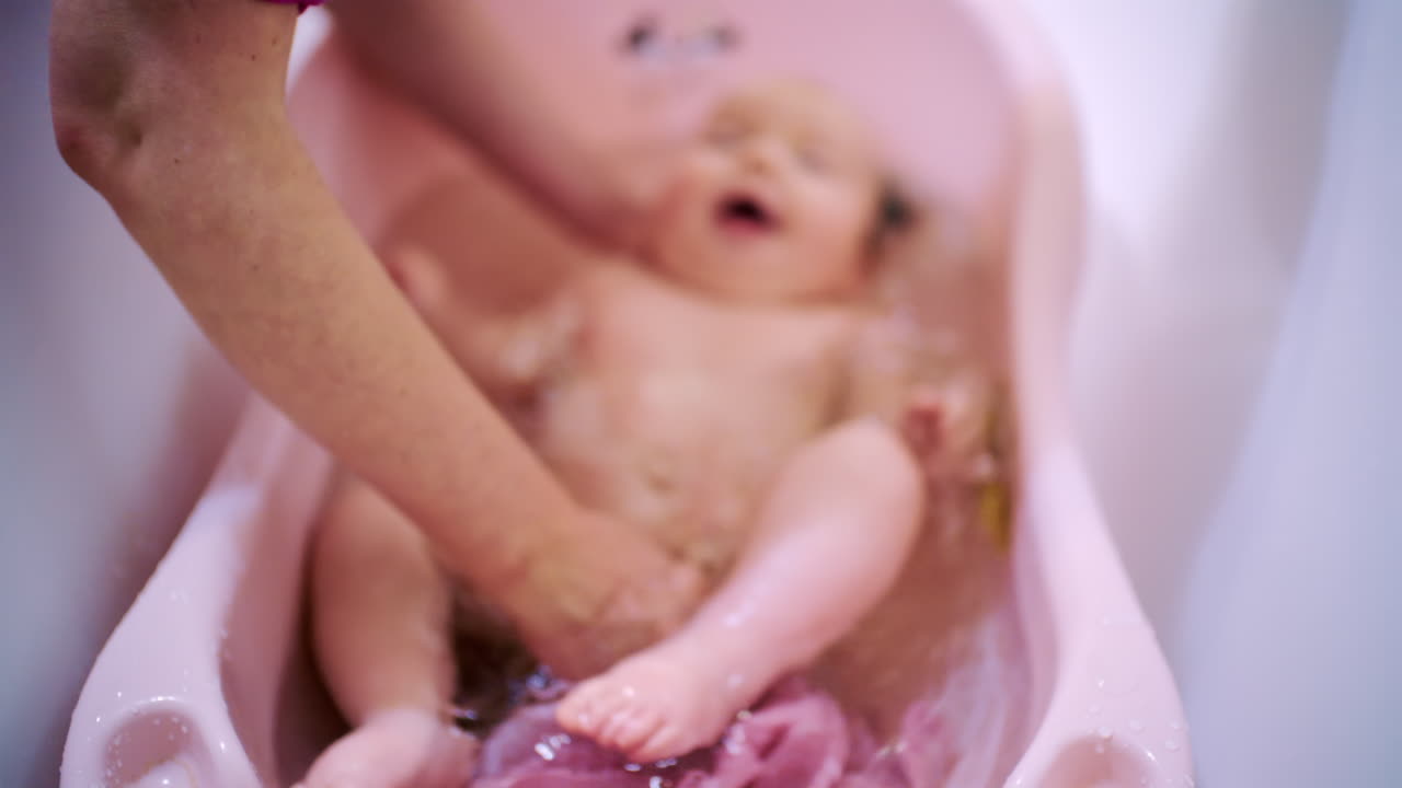 Bebé recién nacido bañándose en una bañera infantil mientras un cuidador lo sostiene y lo lava suavemente