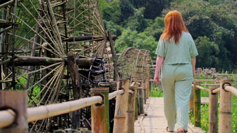 female tourist walking on the wooden footbridge in pu luong ancient waterwheels in vietnam. static shot