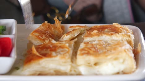una persona corta en un pedazo de pastel turco, un delicioso su böreği, mientras cena en un restaurante