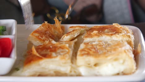 a person cuts into a piece of turkish pastry, a delicious looking su böreği, while dining at a restaurant