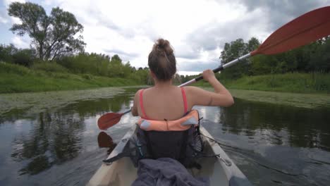 Fit-blonde-strong-woman-paddling-a-Kayak-in-slow-motion-through-river-in-cloudy-day