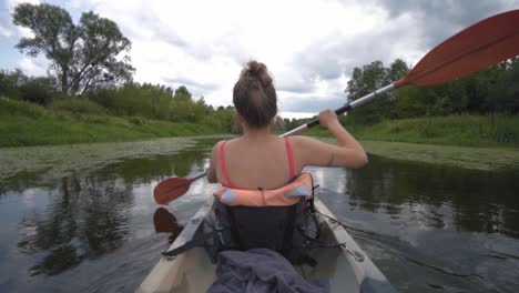 fit blonde strong woman paddling a kayak in slow motion through river in cloudy day