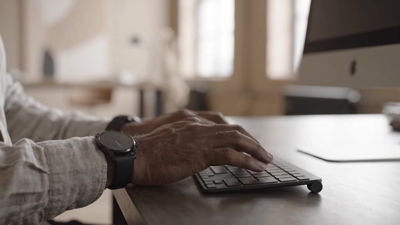Nahaufnahme von Händen, die auf einer modernen Tastatur tippen, die konzentrierte Interaktion in einem eleganten Arbeitsumfeld mit natürlichem Licht und minimalistischem Design zeigt