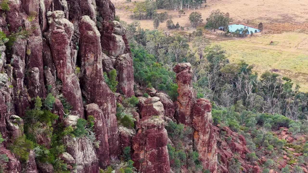 Drone pans across rugged volcanic rock formations and bushland in soft sunset lighting, wide perspective
