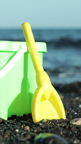 cubo de plástico y pala en una playa de arena negra con el océano en vertical