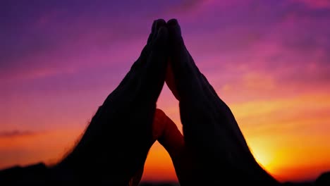 man forms a triangle shape with his hands against a stunning sunset backdrop, creating a moment of tranquility and reflection