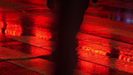 red light reflects against wet road as person cross street in slow motion