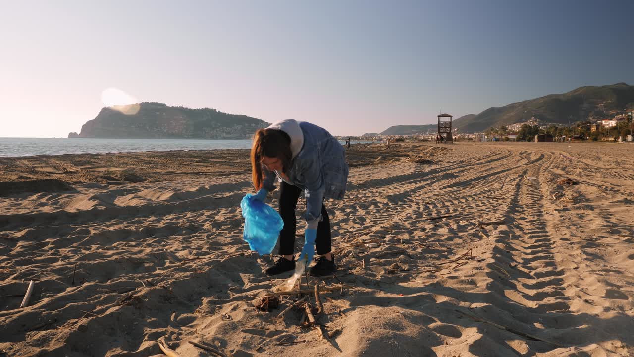 mujer joven recogiendo basura de plástico en la playa. niña limpiando la playa de botellas de plástico y basura. voluntario recogiendo la basura en una bolsa de basura. contaminación plástica y concepto de problema ambiental