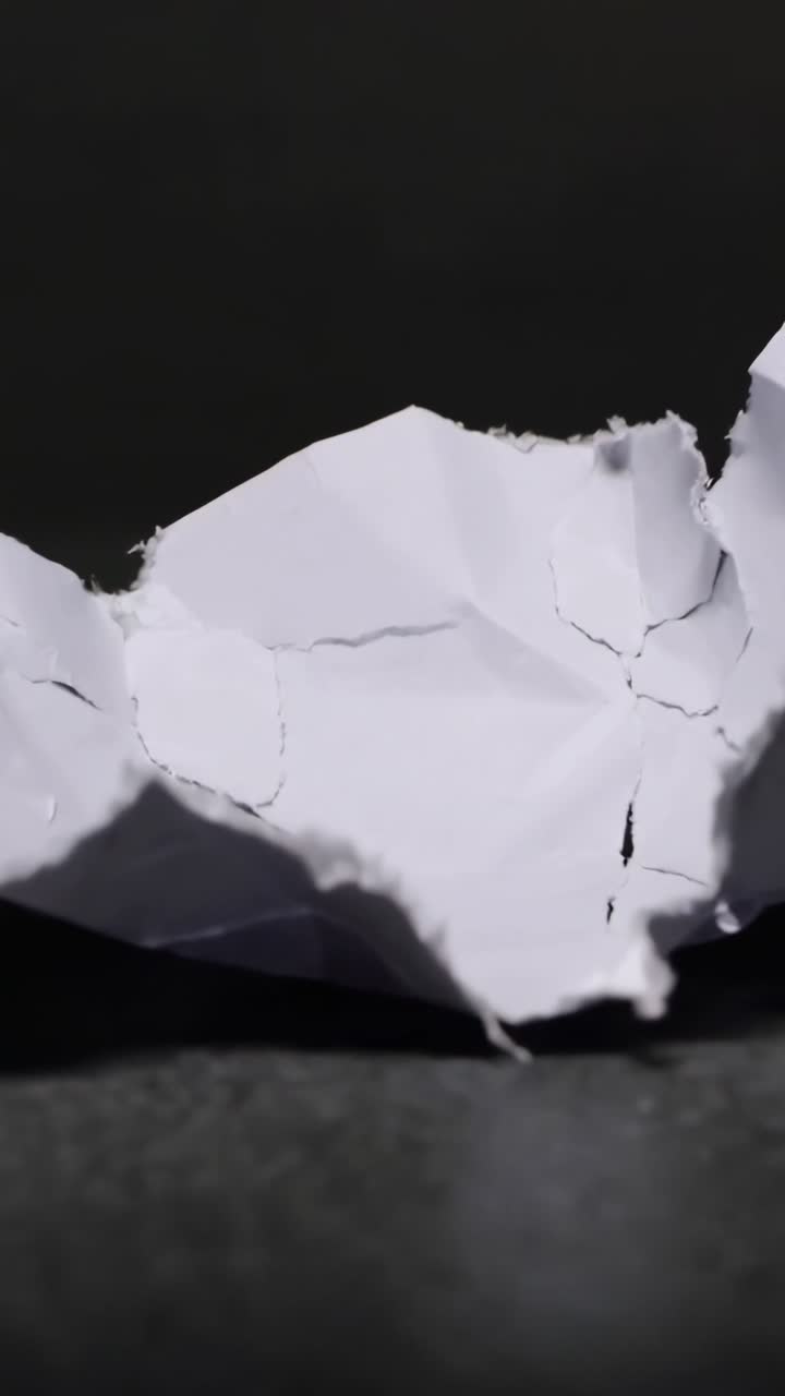 Camera moving forward, revealing crumpled white paper on dark tabletop, lighting showing torn edges