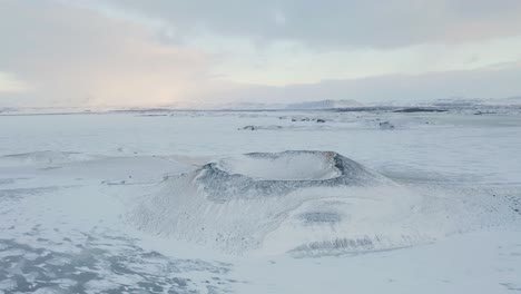 Aerial-flyover-Snowy-volcano-Crater-and-frozen-snowcapped-My-vatn-Lake-during-beautiful-day-in-Iceland