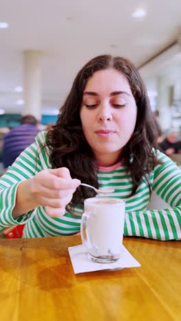 a woman is sitting at a table with a cup of coffee and a spoon