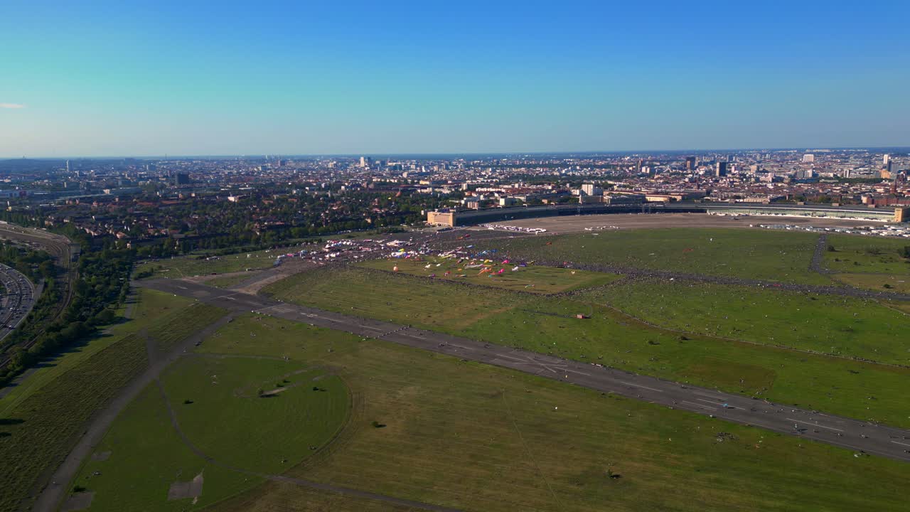 thousands of Berliners enjoying the giant kite festival on a sunny day at Tempelhofer Feld, the former Tempelhof Airport. Dramatic aerial view flight drone shot from above