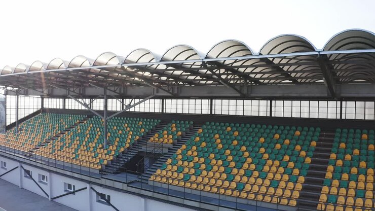 Empty football tribune with green and yellow seats on sunny day - Aerial drone view
