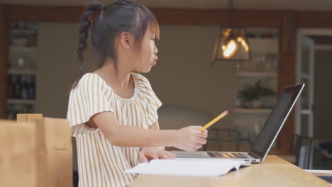 young asian girl home schooling working at table using laptop