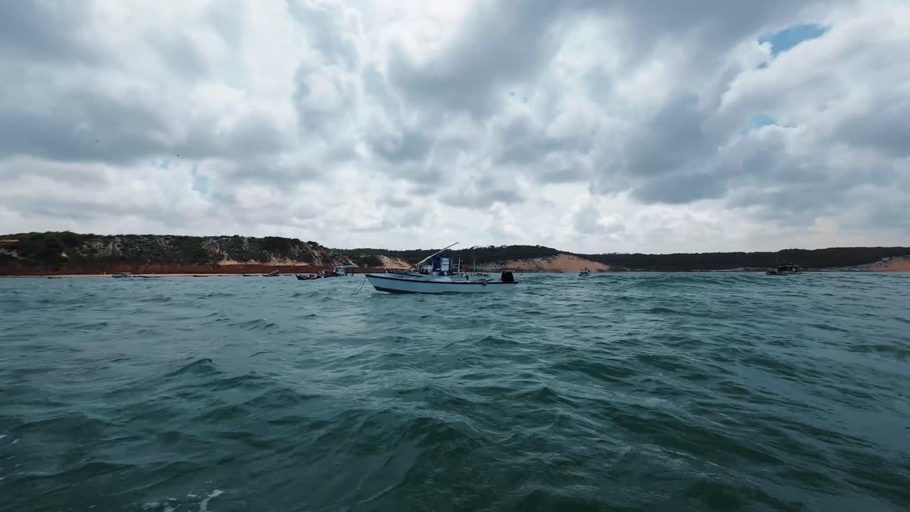 cámara de acción panorámica filmada en la parte superior de un pequeño barco de pesca que navega entre barcos atracados en la playa de cacimba en la famosa ciudad de playa de surf de baia formosa en rio grande do norte, brasil en un día de verano