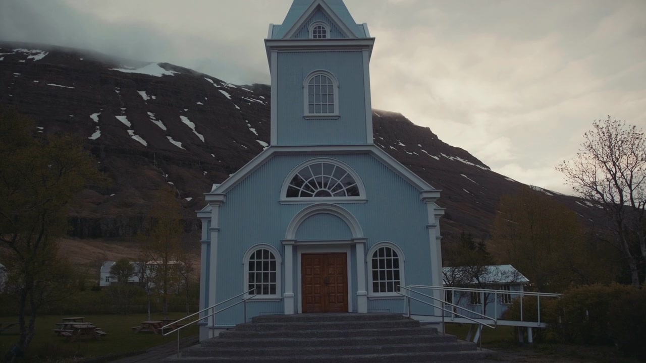 Lys blå kirke i en naturskjønn islandsk fjord med snødekte fjell