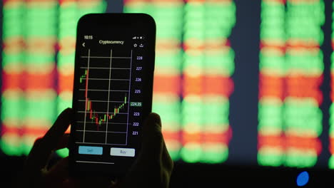 hands with a mobile phone checking stock market data. mobile phone stock exchange. graphs and tables in the background