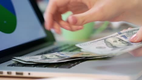 mujer contando billetes de dólares con la mano en el teclado de la computadora portátil. . dinero de negocios en línea