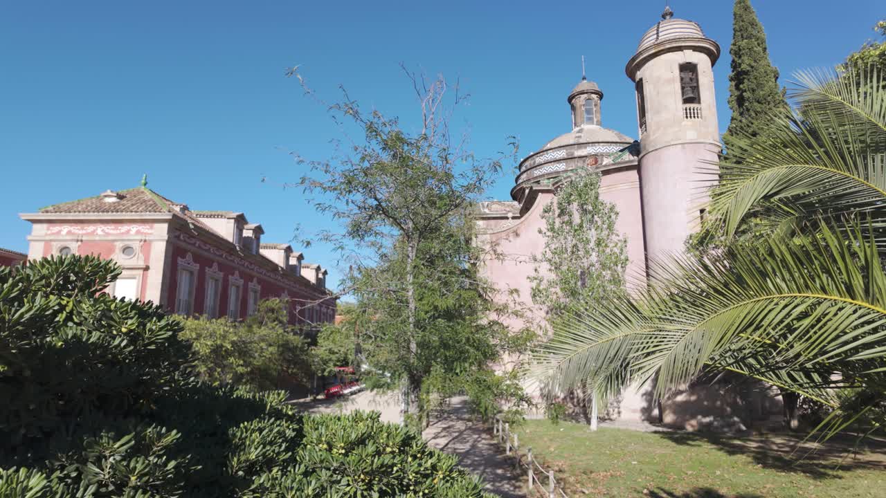 una histórica iglesia militar de ciudadela con arquitectura distintiva se encuentra en medio de exuberantes jardines verdes bajo un cielo azul soleado, ofreciendo una atmósfera pacífica.