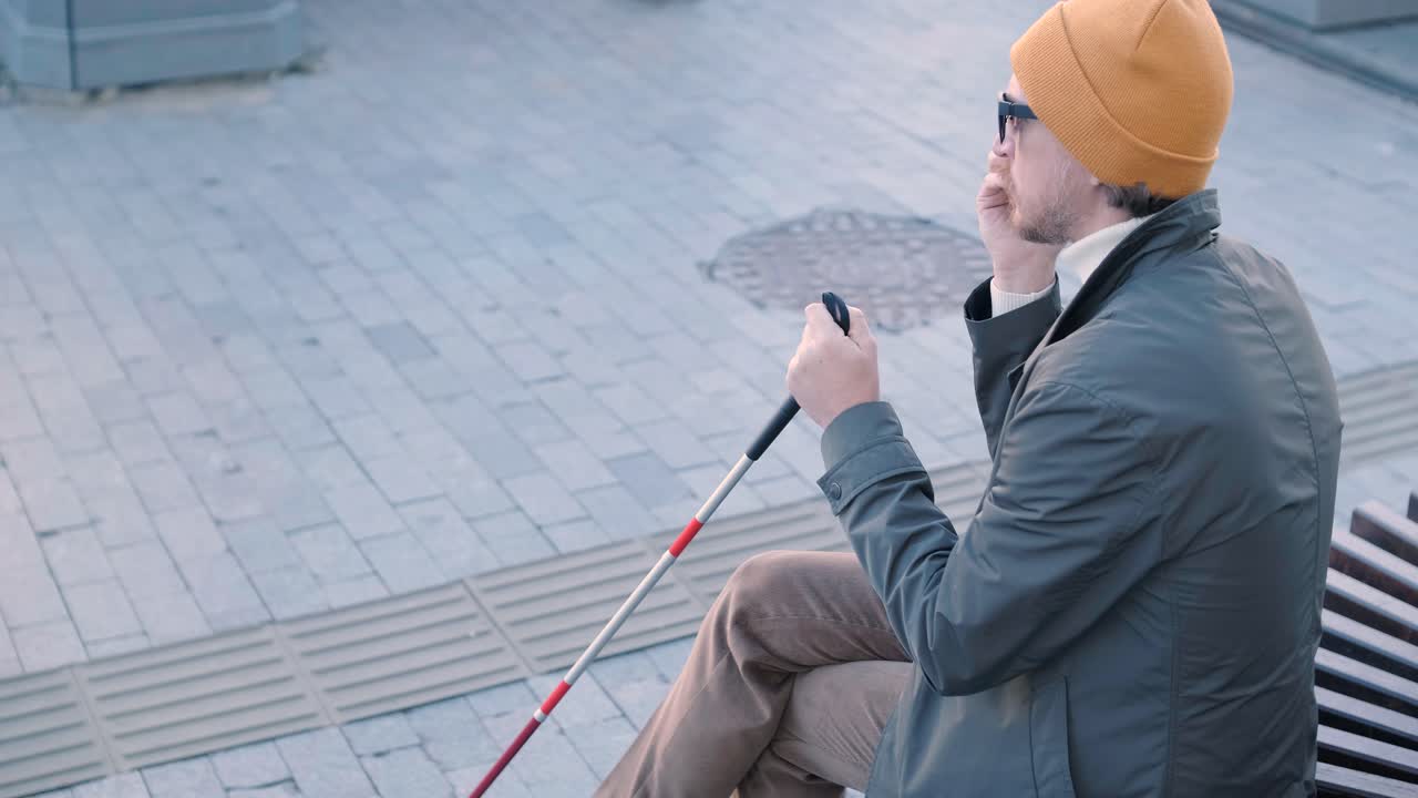 도시 공원 의 벤치 에 앉아 스마트폰 을 들고 있는 눈먼 젊은이 가 전화 하고 있다