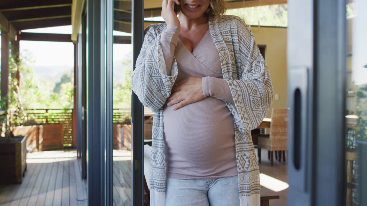 Happy caucasian pregnant woman standing on patio and having phone call