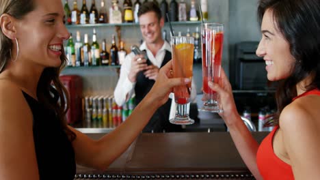 Young-women-toasting-cocktail-glasses-at-bar-counter