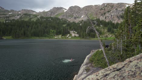 Young-male-with-dog-leaps-into-cold-mountain-lake-under-overcast-sky