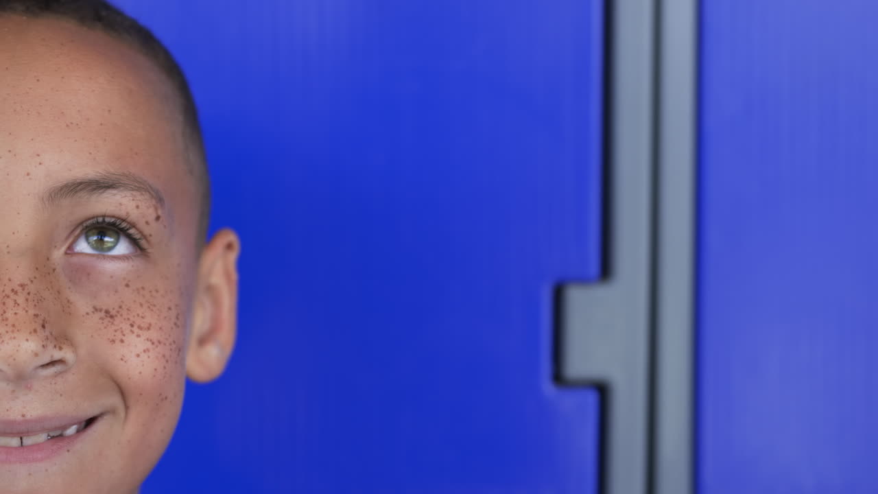 Biracial boy with freckles smiles against a vibrant blue background with copy space in school