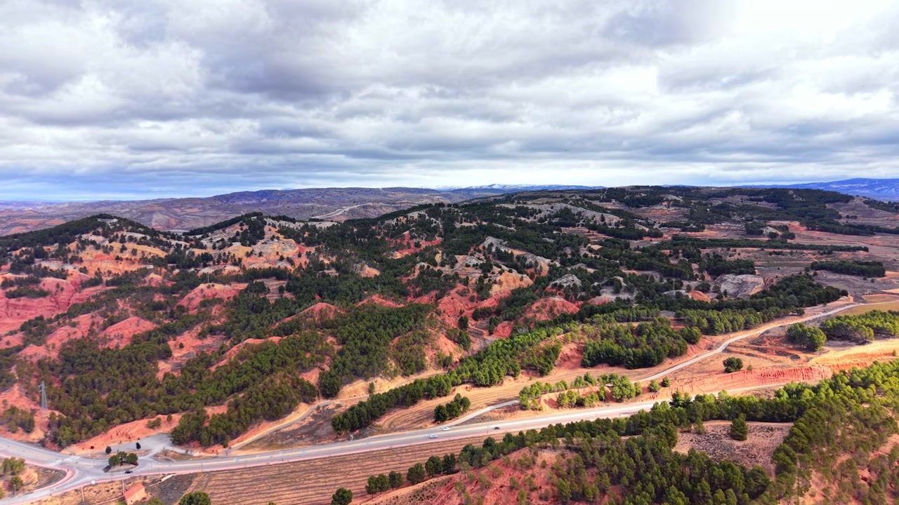Paisagem natural de formações de solo vermelho erodido misturadas com florestas de pinheiros verdes sob céu nublado. Vista panorâmica de colinas de argila vermelha e árvores verdes.