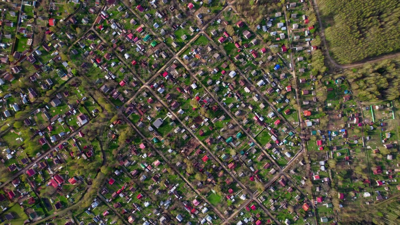 Vertical drone view captures village street grid garden plots small houses and dense forest edge for rural planning land use residential pattern and countryside texture