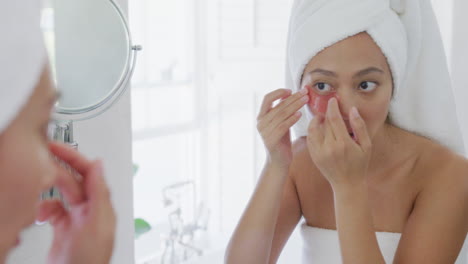 mujer asiática feliz mirándose en el espejo y aplicando parches oculares en el baño, en cámara lenta